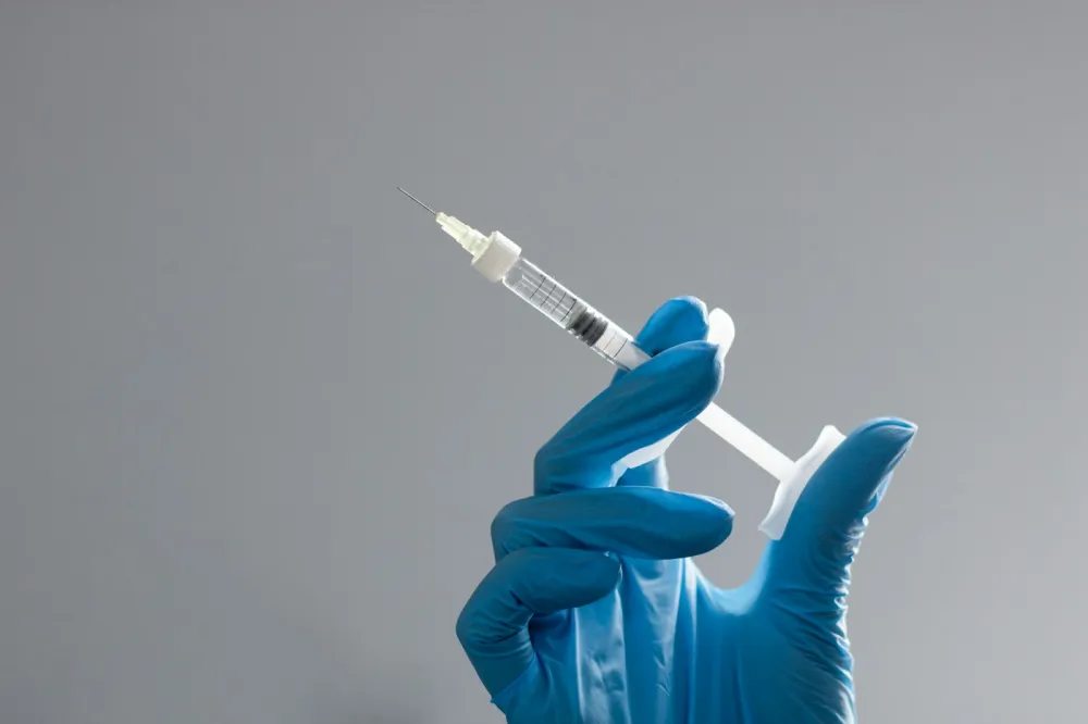 Gloved hand holding an unbranded syringe used for injectable treatments